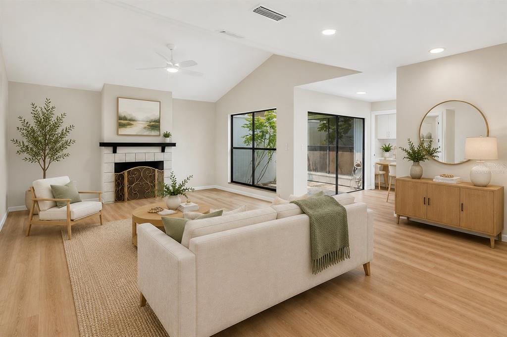 A living room with a fireplace, vaulted ceiling, light wood floors, and neutral furniture — 647 BONNIE BOULEVARD, PALM HARBOR, FL