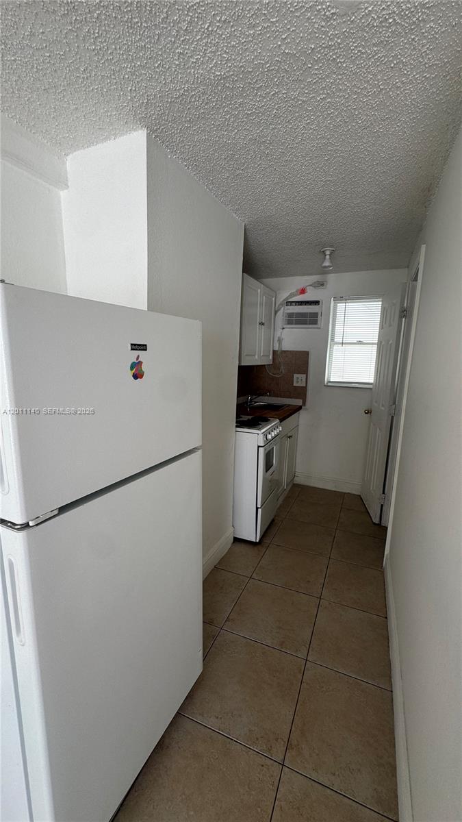 A narrow kitchen features white appliances, tiled flooring, and a window with a wall unit — 921 N 17th Ct # 927, Hollywood FL 33020, HOLLYWOOD, FL