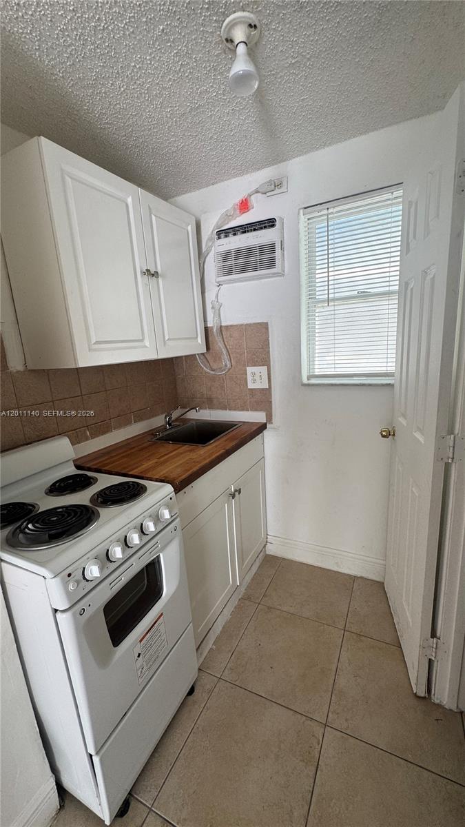 A small kitchen features white cabinets, a wooden countertop, a stove, and a window — 921 N 17th Ct # 927, Hollywood FL 33020, HOLLYWOOD, FL