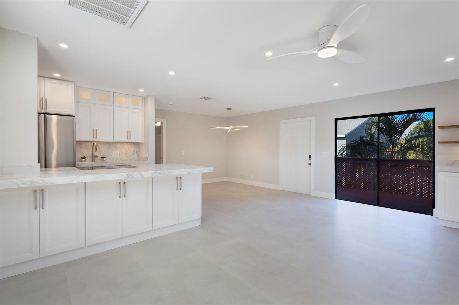 A modern kitchen with white cabinets, marble countertops, and a sliding glass door to a balcony — 7 Crossings Circle, Boynton Beach FL 33435, BOYNTON BEACH, FL