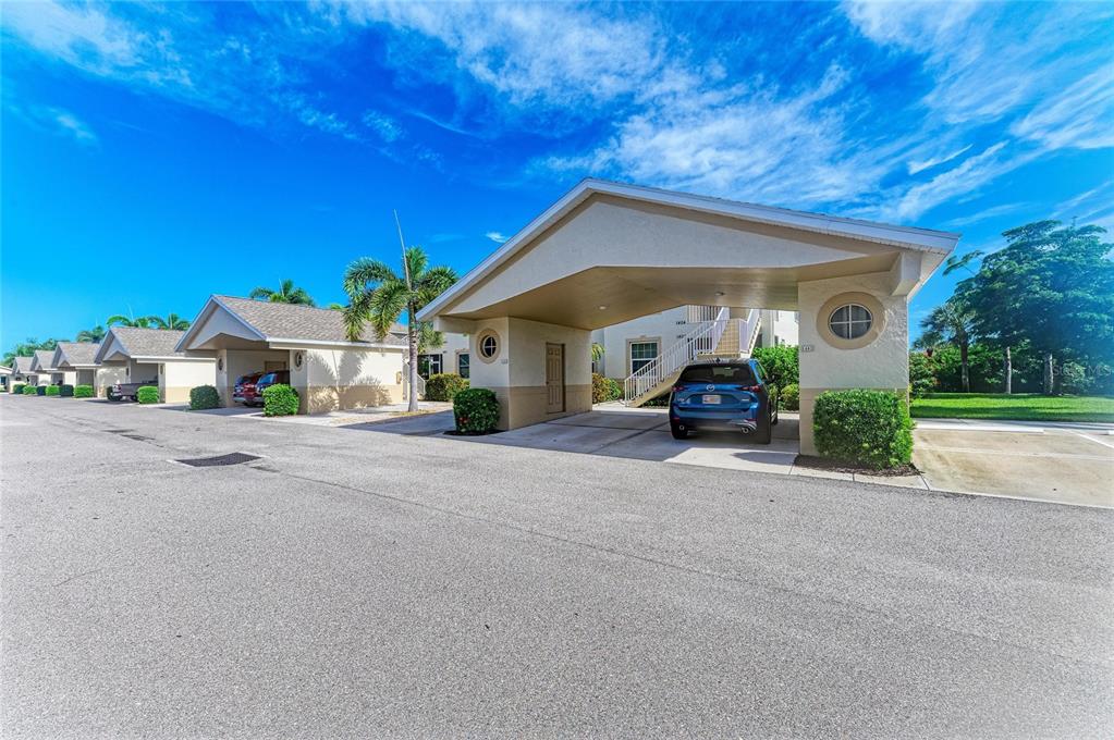A blue car is parked under a covered carport attached to a multi-unit residential building — 1404 AUBURN LAKES CIRCLE UNIT 4, VENICE, FL