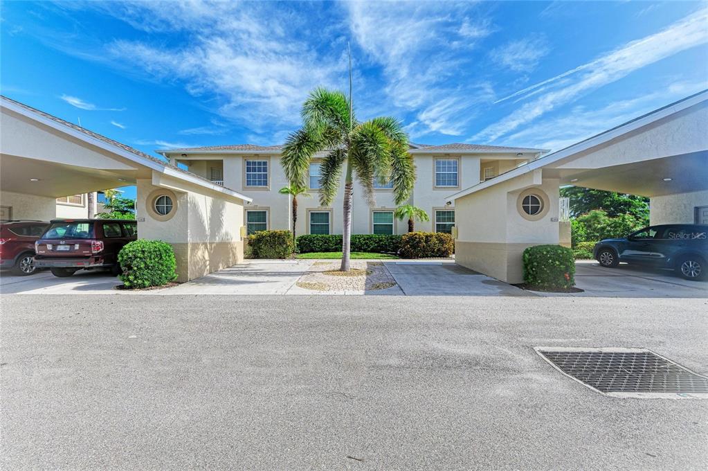The exterior of a two-story apartment building features covered parking spaces and a central palm tree — 1404 AUBURN LAKES CIRCLE UNIT 4, VENICE, FL