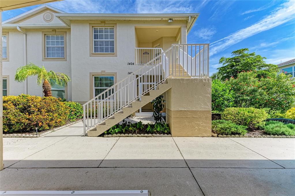 A two-story apartment building features a concrete staircase leading to an upper-level balcony — 1404 AUBURN LAKES CIRCLE UNIT 4, VENICE, FL