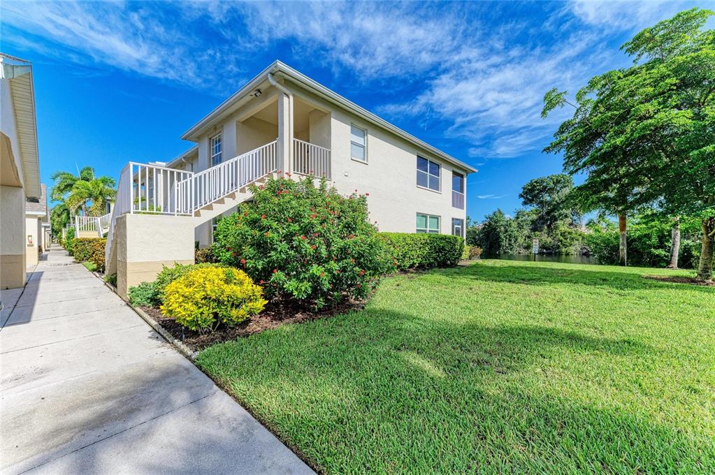 A two-story apartment building with exterior stairs, a grassy lawn, and surrounding trees — 1404 AUBURN LAKES CIRCLE UNIT 4, VENICE, FL
