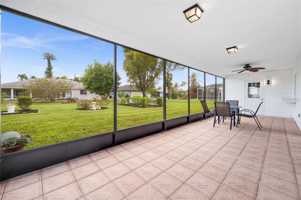 A screened-in patio with tiled flooring overlooks a grassy backyard with trees and neighboring houses — 706 SW 51ST TERRACE, CAPE CORAL, FL