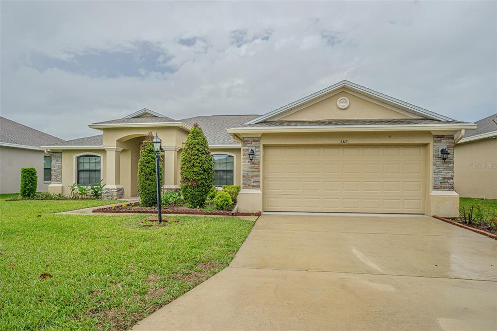 A single-story suburban house with a tan stucco exterior, stone accents, and a two-car garage — 1311 EVERGREEN PARK CIRCLE, LAKELAND, FL