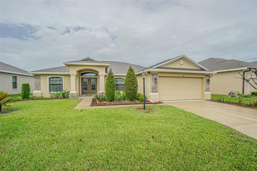A single-story suburban house with a tan stucco exterior, a two-car garage, and a lawn — 1311 EVERGREEN PARK CIRCLE, LAKELAND, FL
