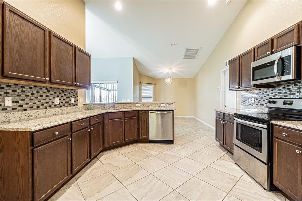 A kitchen with dark wood cabinets, granite countertops, stainless steel appliances, and tiled flooring — 1311 EVERGREEN PARK CIRCLE, LAKELAND, FL