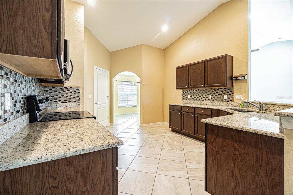 A kitchen with dark wood cabinets, granite countertops, tile backsplash, and light-colored floor tiles — 1311 EVERGREEN PARK CIRCLE, LAKELAND, FL