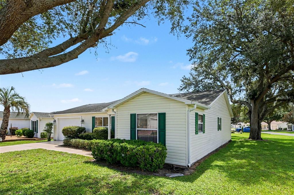 A single-story house with light yellow siding, green shutters, and a large tree in front — 1501 LAS PACOS COURT, THE VILLAGES, FL