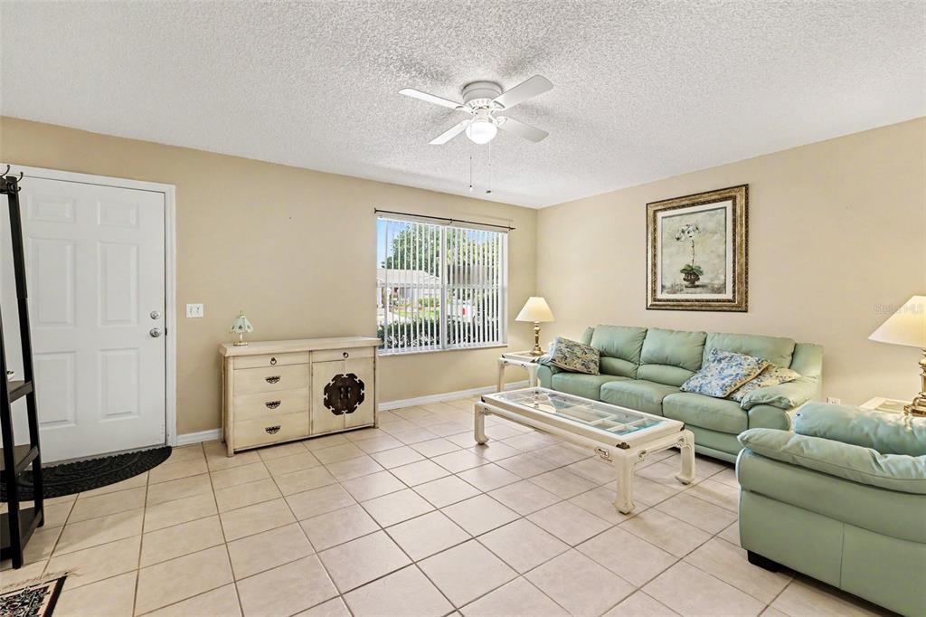 A living room features light tile flooring, a green sofa, and a ceiling fan — 1501 LAS PACOS COURT, THE VILLAGES, FL