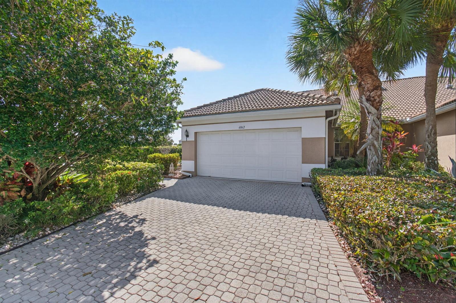 A paved driveway leads to a single-story house with a two-car garage and landscaping — 6862 Swansea Lane, Boynton Beach FL 33472, BOYNTON BEACH, FL
