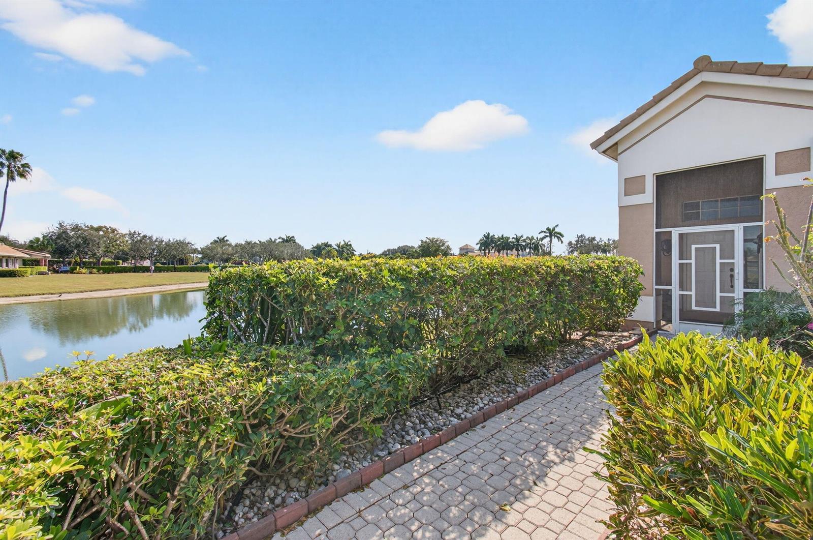 A paved walkway leads past a hedge toward a house entrance overlooking a lake — 6862 Swansea Lane, Boynton Beach FL 33472, BOYNTON BEACH, FL