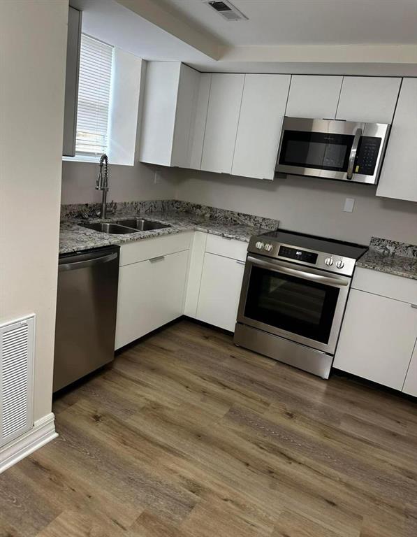 A kitchen features white cabinets, stainless steel appliances, granite countertops, and wood-look flooring — 716 TROPIC STREET, TITUSVILLE, FL
