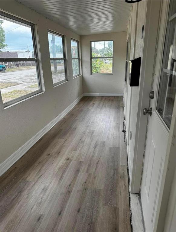 A narrow sunroom features light wood-look flooring, white walls, and multiple windows — 716 TROPIC STREET, TITUSVILLE, FL