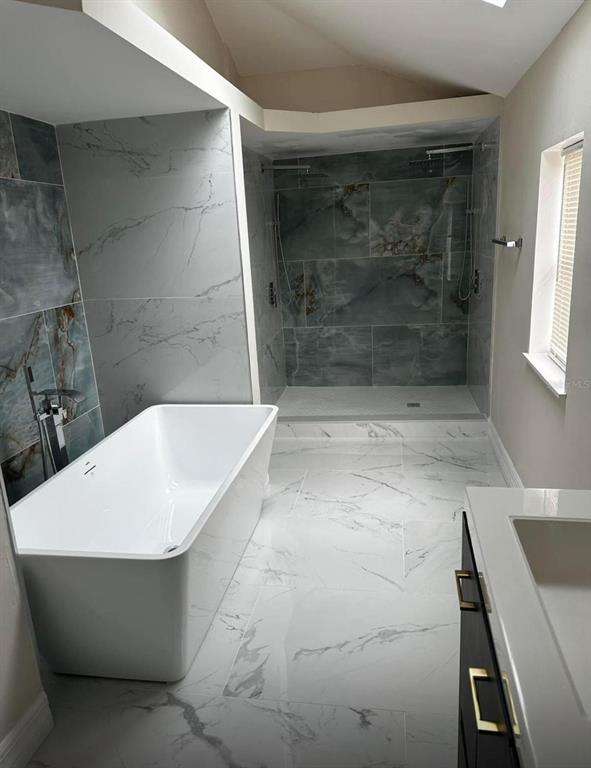 A modern bathroom features a freestanding white tub, a walk-in shower, and marble-look tile flooring — 716 TROPIC STREET, TITUSVILLE, FL