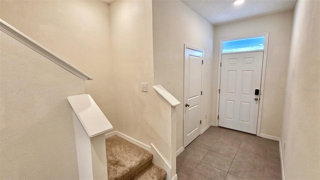 An entryway features a tiled floor, a carpeted staircase, and a white front door — 1737 HOVENWEEP ROAD, WESLEY CHAPEL, FL
