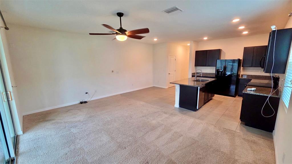 An open-concept living room with carpeted flooring flows into a kitchen featuring dark cabinetry — 1737 HOVENWEEP ROAD, WESLEY CHAPEL, FL