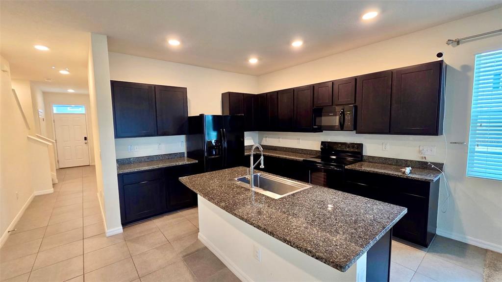 A kitchen features dark cabinets, granite countertops, a center island with a sink, and tile flooring — 1737 HOVENWEEP ROAD, WESLEY CHAPEL, FL