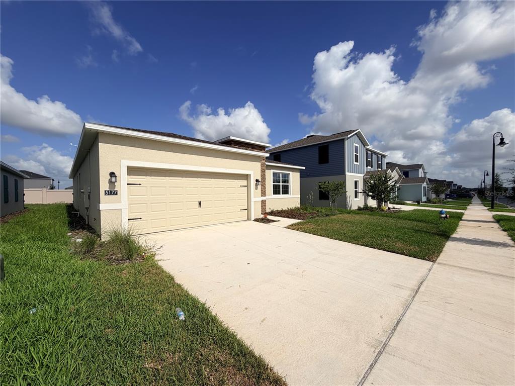 A single-story house with a beige exterior and a two-car garage under a blue sky — 5177 GREEN BELT DRIVE, HAINES CITY, FL