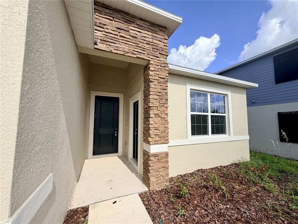 A beige house exterior features a stone-accented pillar, a dark front door, and a window — 5177 GREEN BELT DRIVE, HAINES CITY, FL