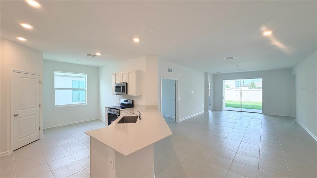 An open-concept kitchen and living area features light tile flooring, white cabinetry, and sliding glass doors — 5177 GREEN BELT DRIVE, HAINES CITY, FL