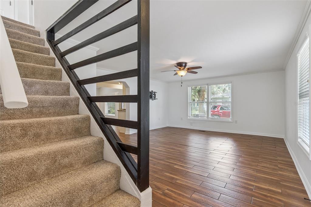 A carpeted staircase with a black railing overlooks a living room with wood-look tile flooring — 306 S DISSTON AVENUE, MINNEOLA, FL