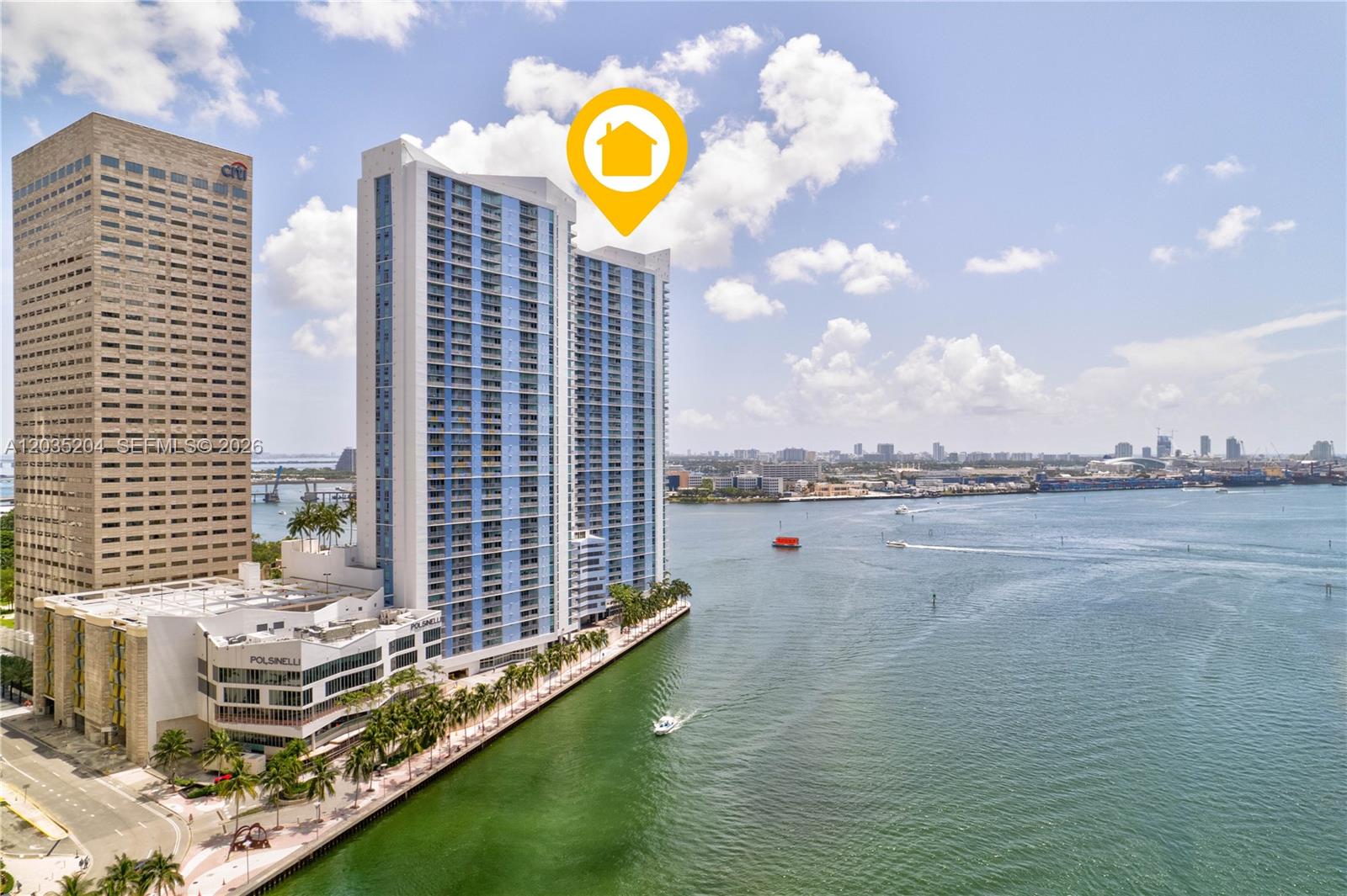 An aerial view shows a tall blue residential tower situated along a waterfront promenade — 335 S Biscayne Blvd # 3108, Miami FL 33131, MIAMI, FL