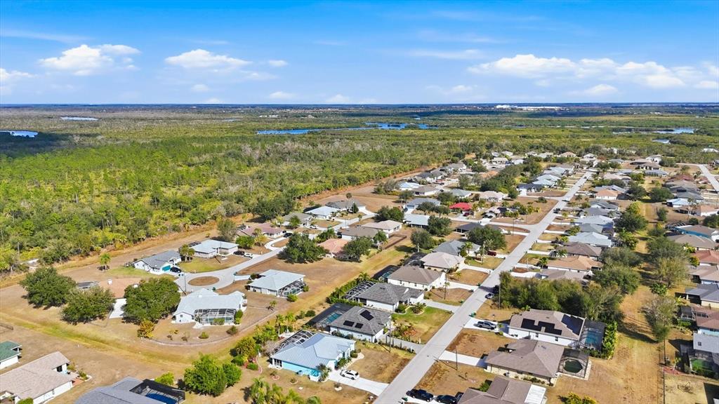 An aerial view shows a suburban neighborhood with single-family homes surrounded by dense green vegetation — 27052 TIERRA DEL FUEGO CIRCLE, PUNTA GORDA, FL