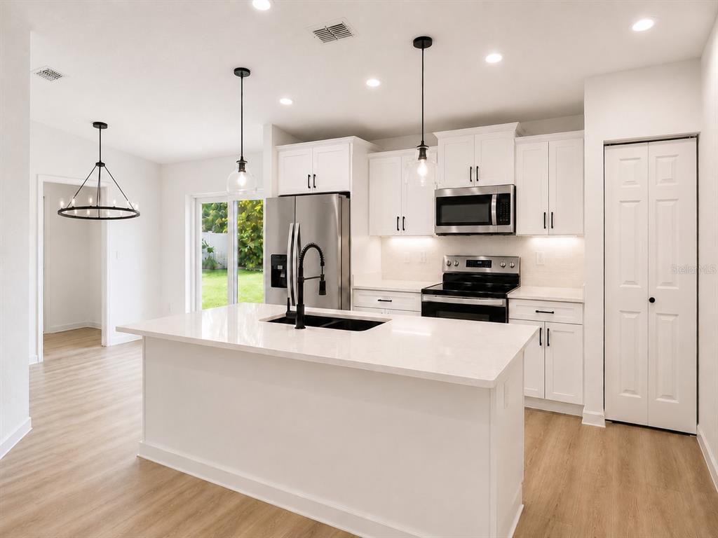 An open-concept kitchen and living area features light wood flooring, white cabinetry, and stainless appliances — 14575 SW 20TH PLACE, OCALA, FL