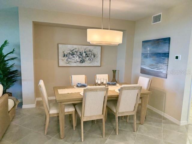 A dining room features a light wood table with six upholstered chairs under a modern chandelier — 17735 BORACAY COURT UNIT 101, VENICE, FL