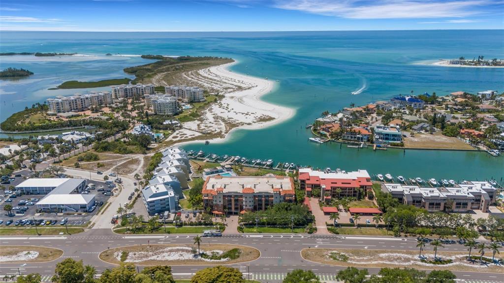 An aerial view shows a coastal residential area with multi-story buildings, a marina, and beaches — 1090 PINELLAS BAYWAY S UNIT A5, ST PETERSBURG, FL