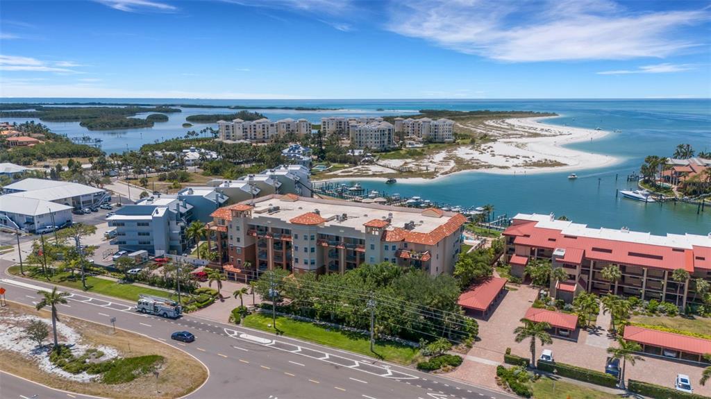 An aerial view shows multi-story residential buildings near a coastal inlet and sandy beach — 1090 PINELLAS BAYWAY S UNIT A5, ST PETERSBURG, FL