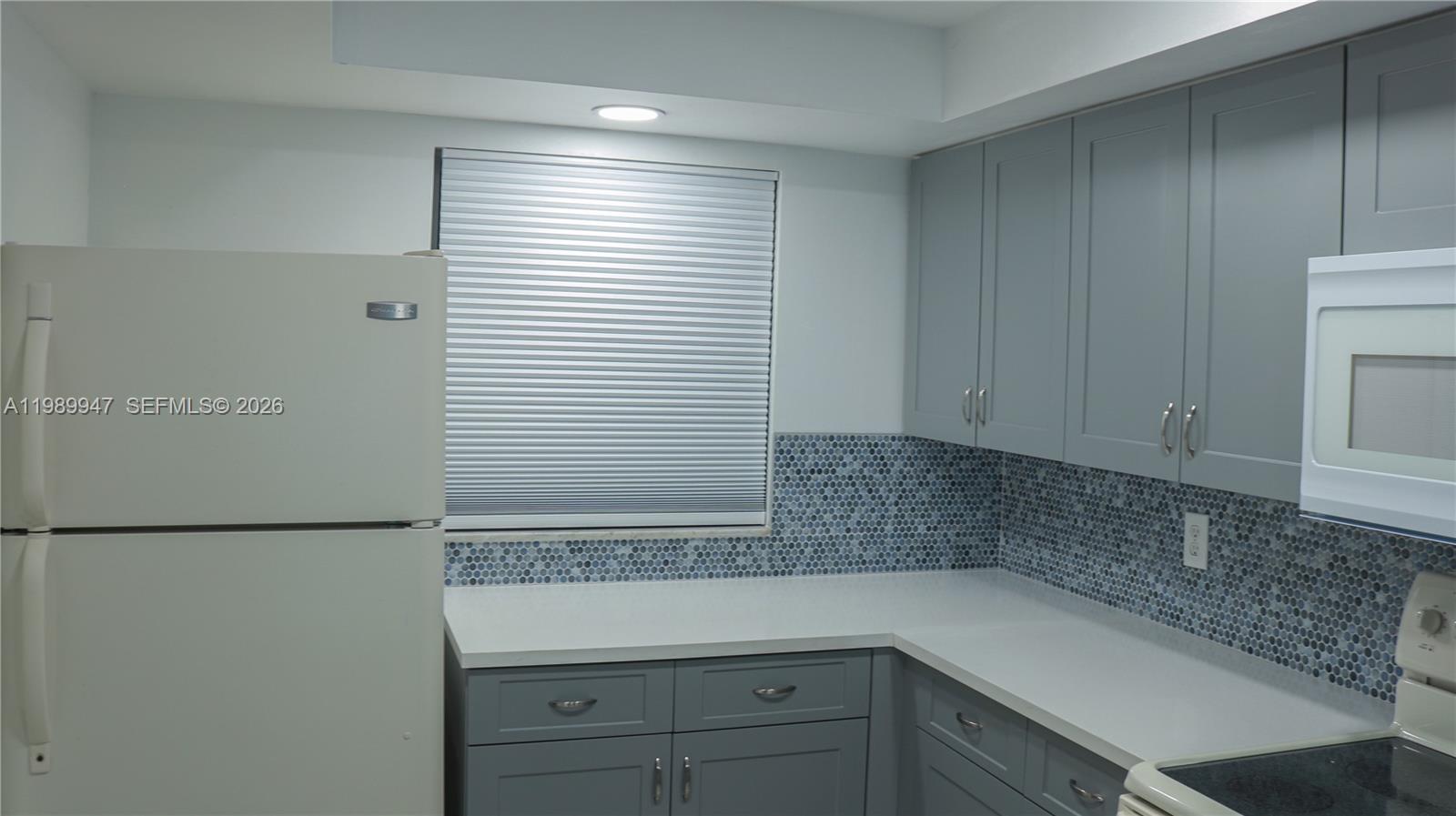 A kitchen features gray cabinets, a white refrigerator, a white countertop, and a blue-tiled backsplash — 9421 Evergreen Pl # 103, Davie FL 33324, DAVIE, FL