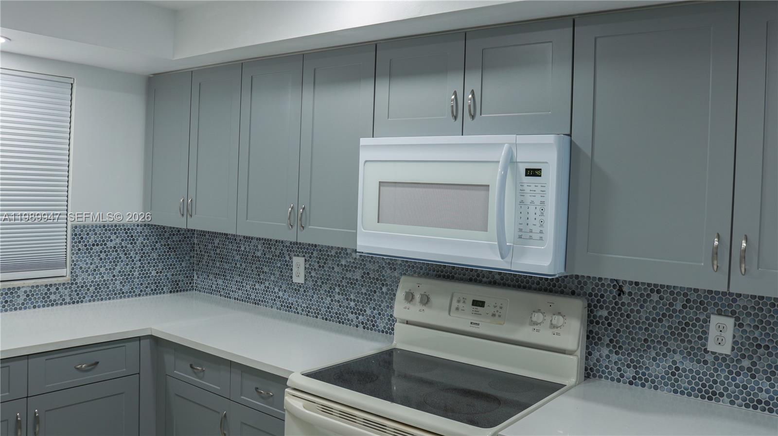 A kitchen features gray cabinets, a white microwave, a white stove, and a mosaic backsplash — 9421 Evergreen Pl # 103, Davie FL 33324, DAVIE, FL