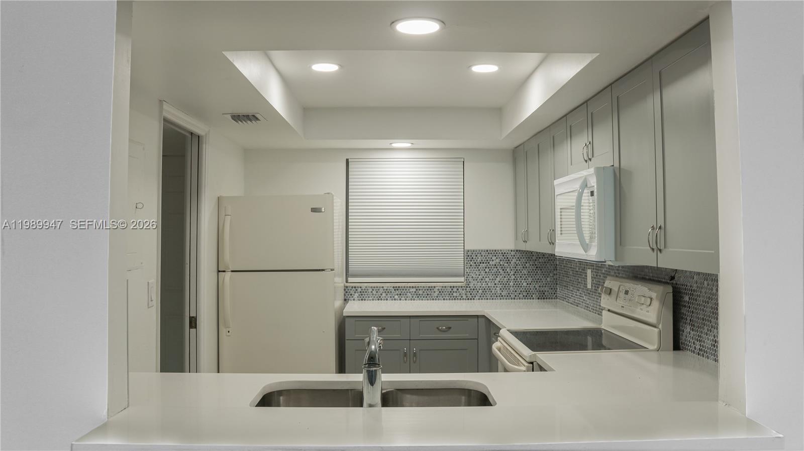 A kitchen features gray cabinets, white countertops, a mosaic backsplash, and white appliances — 9421 Evergreen Pl # 103, Davie FL 33324, DAVIE, FL