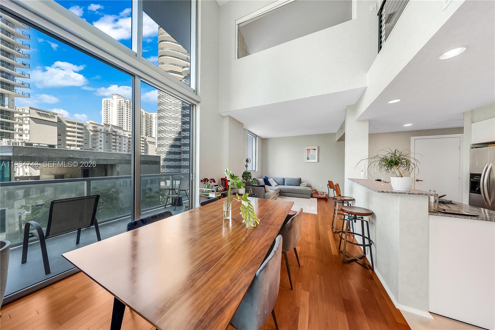 A high-ceilinged dining and living area features hardwood floors, floor-to-ceiling windows, and a balcony — 1050 Brickell Ave # 422, Miami FL 33131, MIAMI, FL