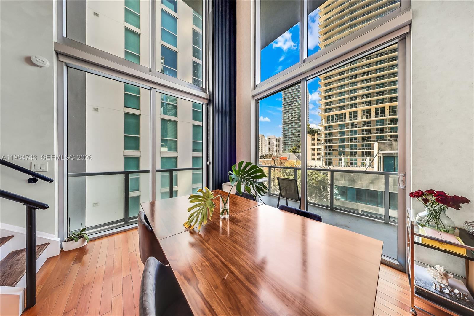 A dining area features a wooden table, floor-to-ceiling windows, and views of city buildings — 1050 Brickell Ave # 422, Miami FL 33131, MIAMI, FL