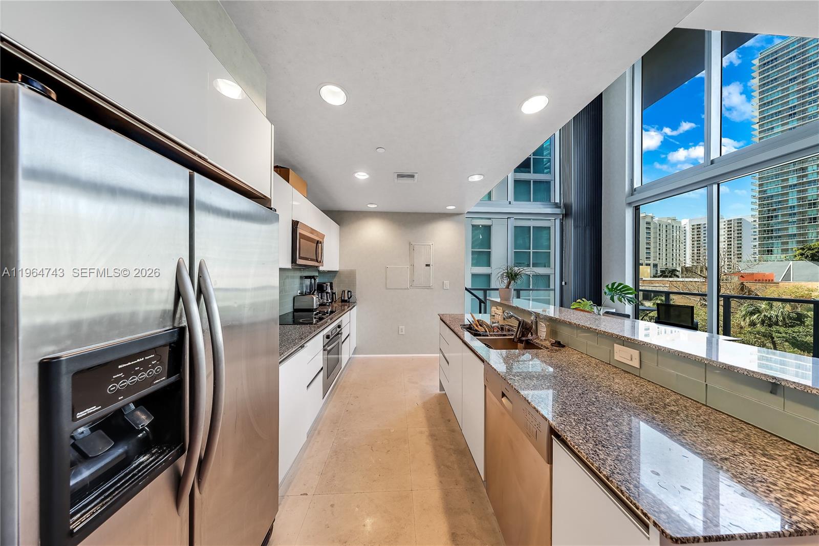 A modern kitchen features stainless steel appliances, granite countertops, and floor-to-ceiling windows with city views — 1050 Brickell Ave # 422, Miami FL 33131, MIAMI, FL