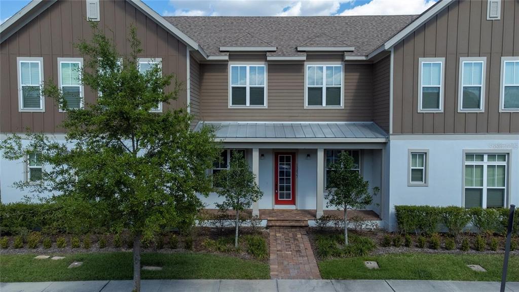 A two-story townhouse with a red front door, brown vertical siding, and a brick walkway — 13427 STODDART AVENUE, ORLANDO, FL
