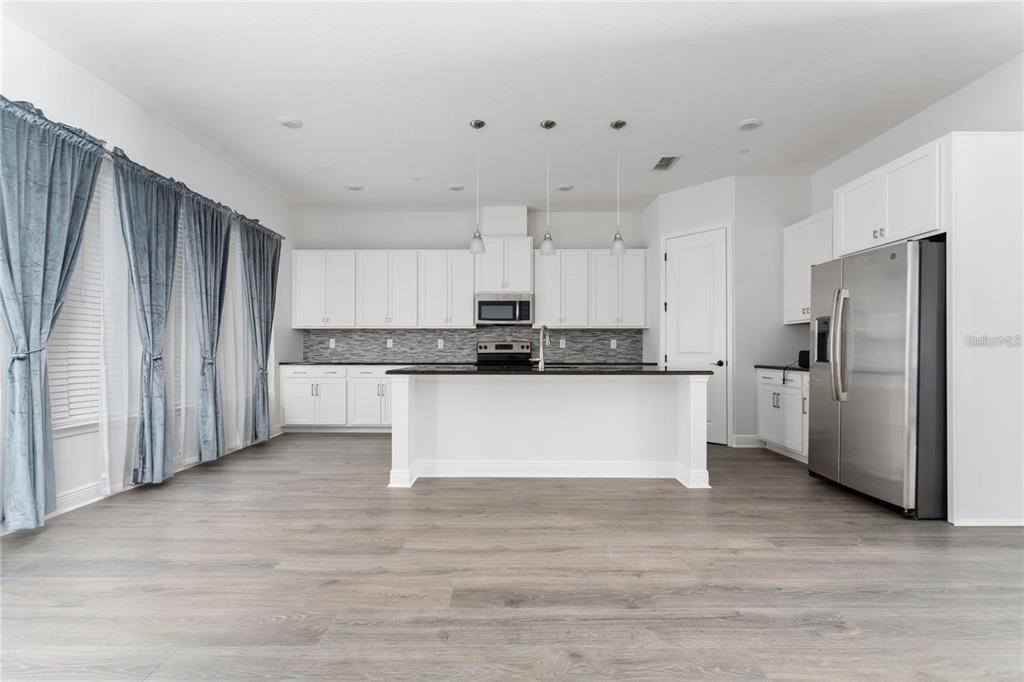 A modern kitchen features white cabinetry, a central island, stainless steel appliances, and gray flooring — 13427 STODDART AVENUE, ORLANDO, FL
