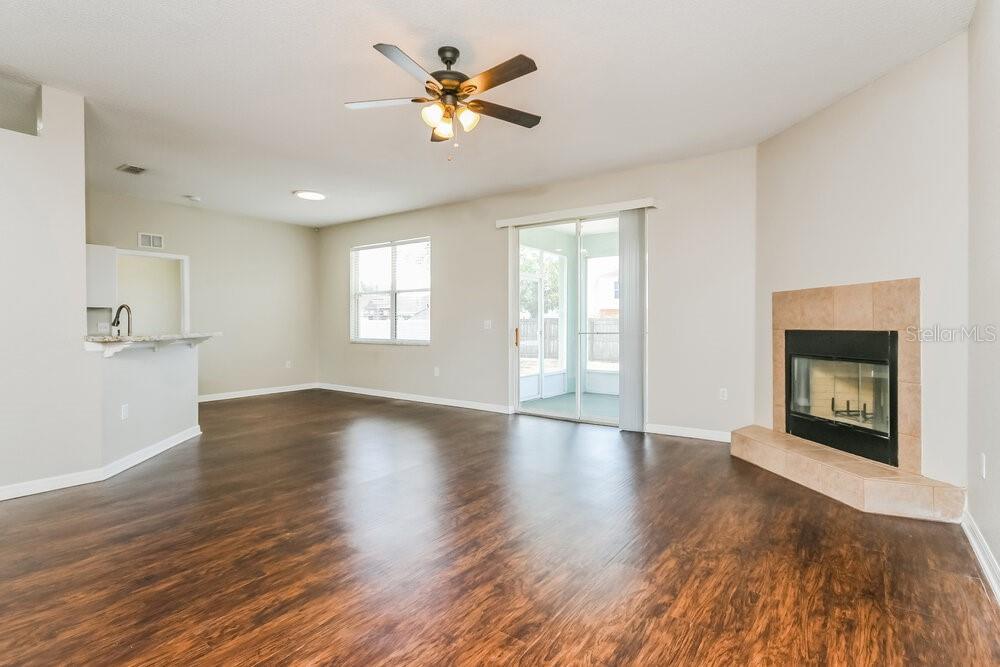 An open living room features dark wood-look flooring, a ceiling fan, and a corner fireplace — 6033 LIVE OAK DRIVE, WINTER HAVEN, FL