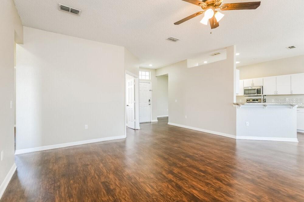An open-concept living area features wood-look flooring, white walls, and a kitchen with white cabinets — 6033 LIVE OAK DRIVE, WINTER HAVEN, FL