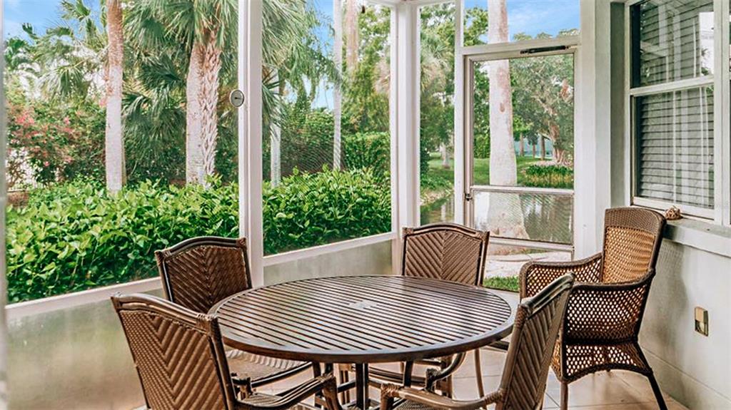 A screened-in patio features a round wooden table with four wicker chairs overlooking lush greenery — 1272 SIESTA BAYSIDE DRIVE UNIT 1272-C, SARASOTA, FL