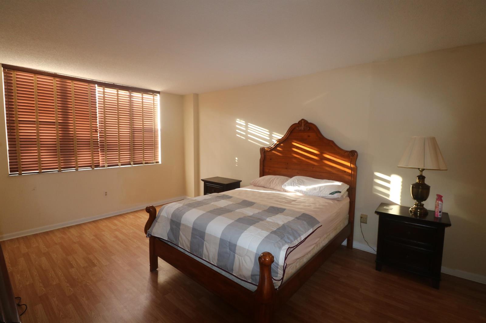 A bedroom features a wooden bed frame, two nightstands, and wood-look flooring under a window — 4001 Hillcrest Drive # 510, Hollywood FL 33021, HOLLYWOOD, FL