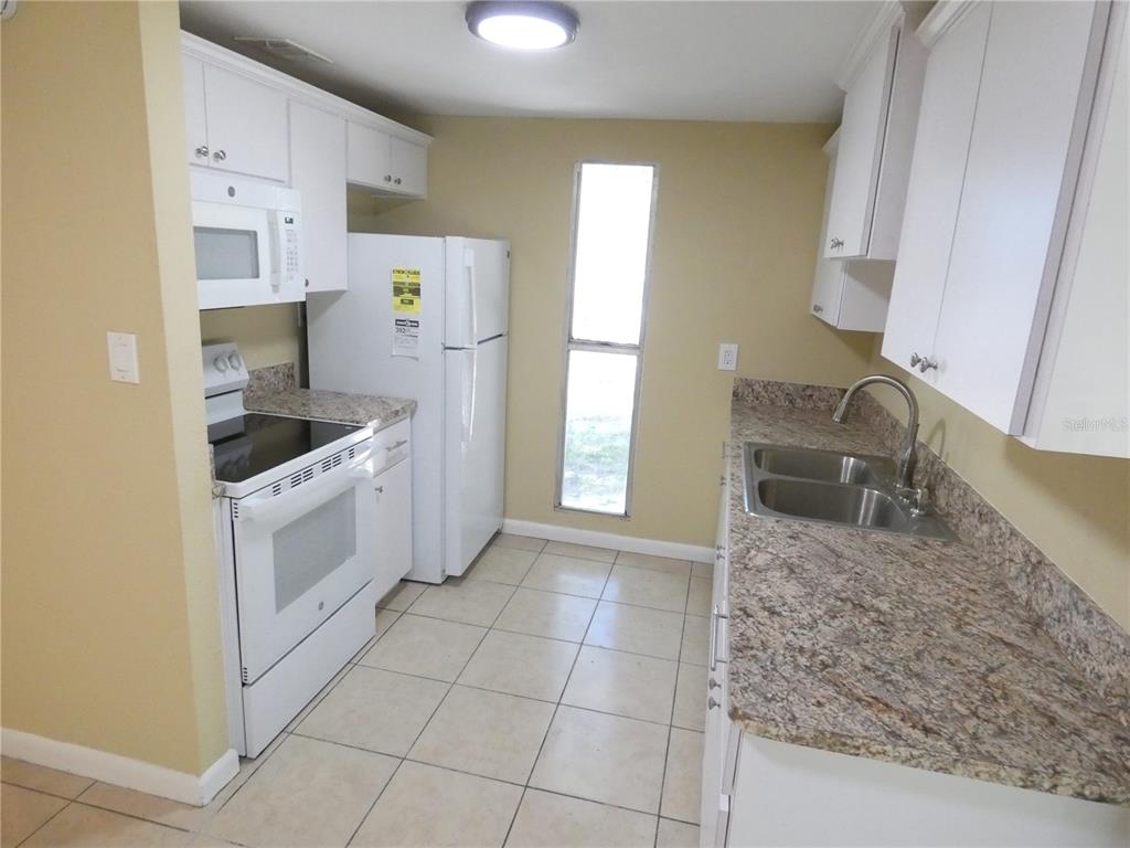 A kitchen features white cabinetry, granite countertops, a double sink, and white appliances — 4410 E 25TH AVENUE, TAMPA, FL