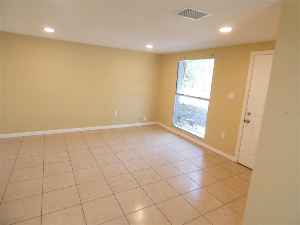 An empty room features tan walls, beige tile flooring, recessed lighting, and a large window — 4410 E 25TH AVENUE, TAMPA, FL