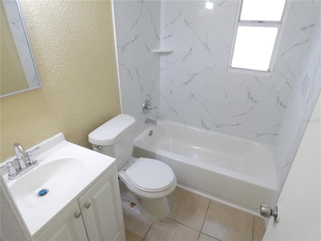 A bathroom with a white vanity, toilet, and a bathtub with marble-patterned wall tiles — 4410 E 25TH AVENUE, TAMPA, FL