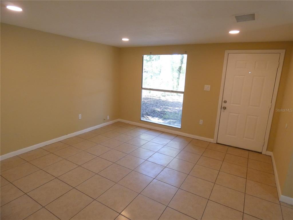 An empty room features tan walls, beige tile flooring, a single window, and a white door — 4410 E 25TH AVENUE, TAMPA, FL