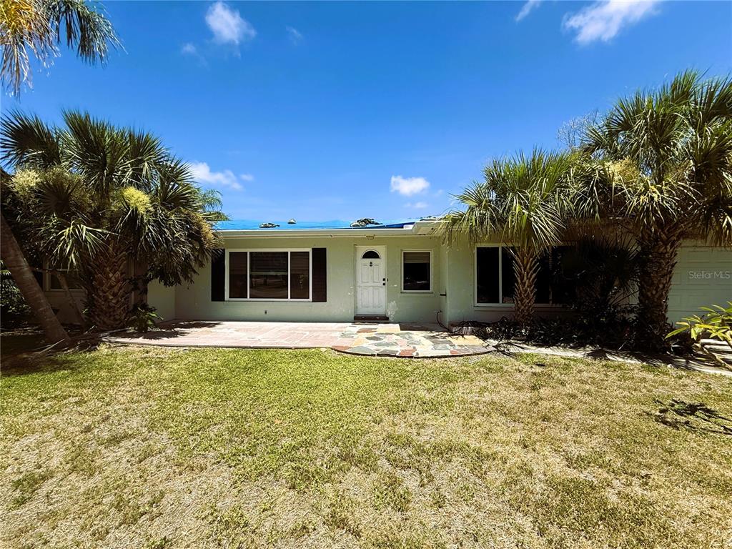 A single-story house with a light green exterior, a blue tarp on the roof, and palm trees — 102 158TH AVENUE, REDINGTON BEACH, FL